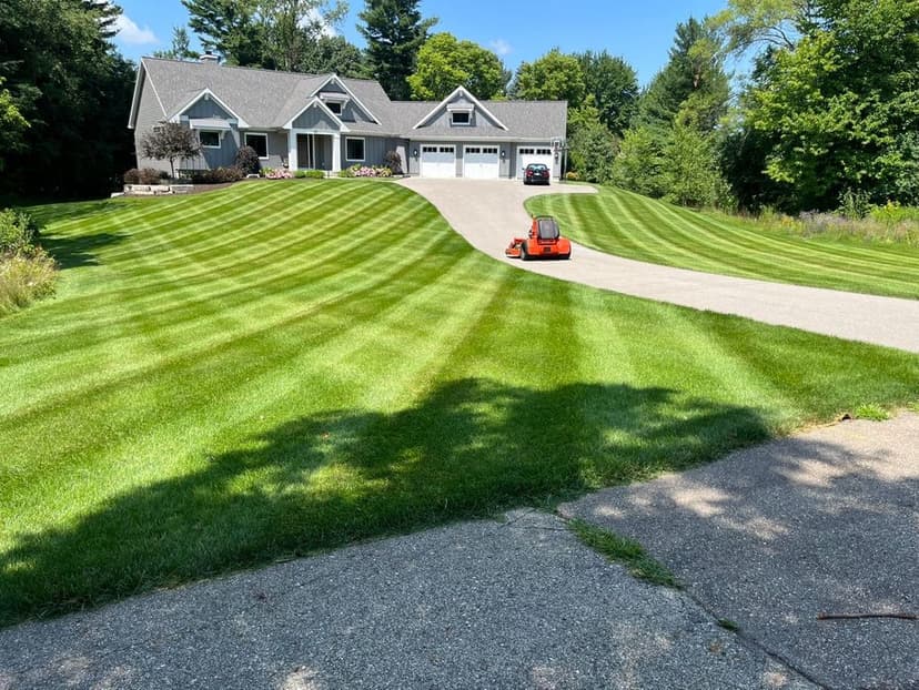 Lawn care scene with striped grass and a house, showcasing neat landscaping and curb appeal.