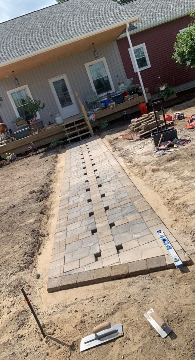 Paved walkway installation in a residential yard leading to a house with a porch.